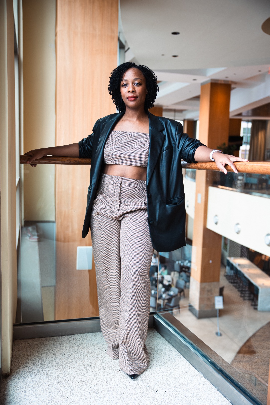 This is a picture of Latesha Lynch, the host of the podcast, leaning against a banister in a power pose with a leather blazer, trousers, and matching cropped top.